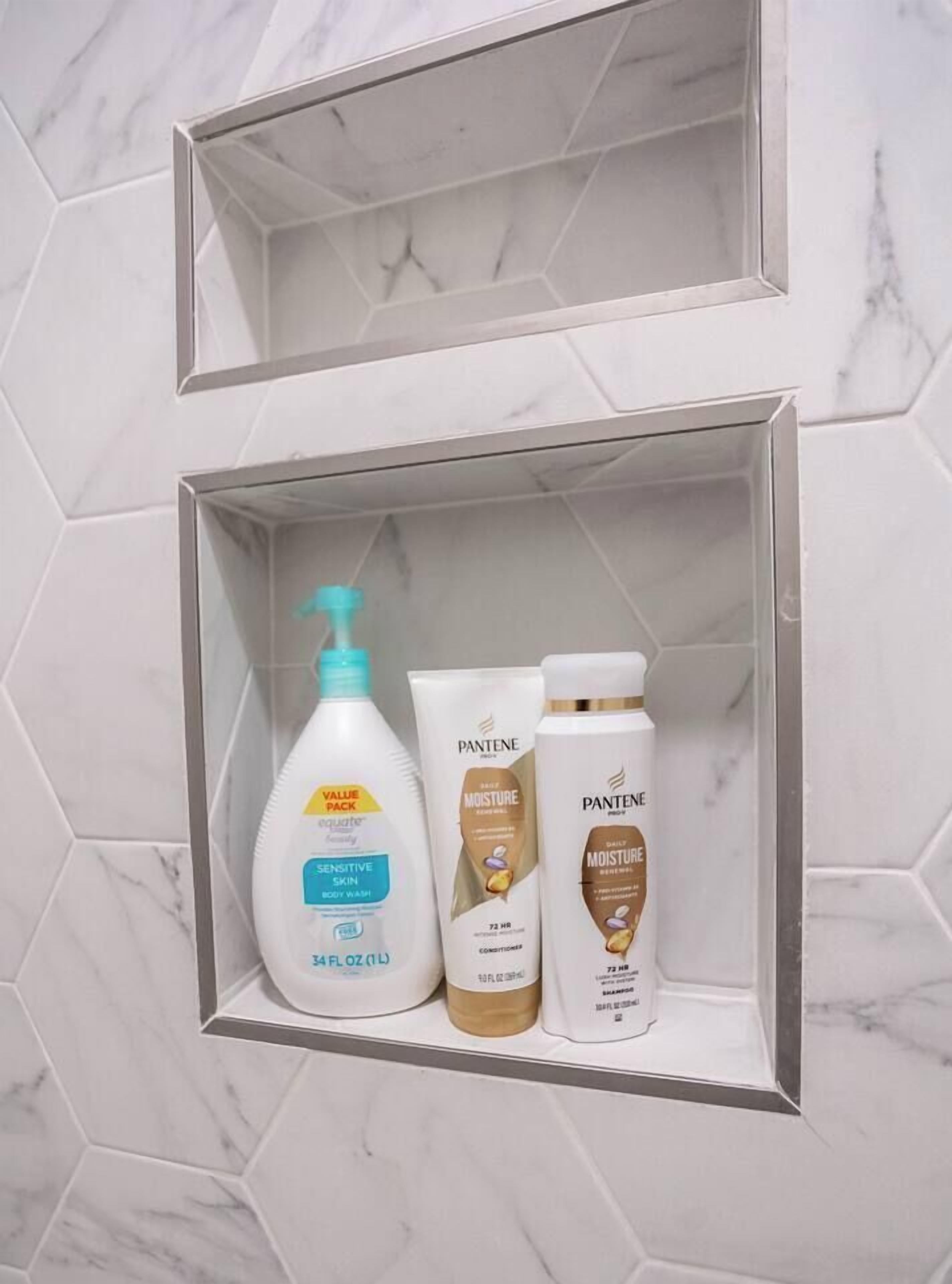 Bany amb paret de rajola de marbre i una estanteria amb tres productes Pantene.