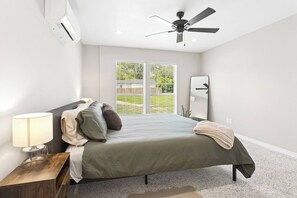 A bedroom with a bed, a nightstand, a lamp, a ceiling fan, and a window with blinds.