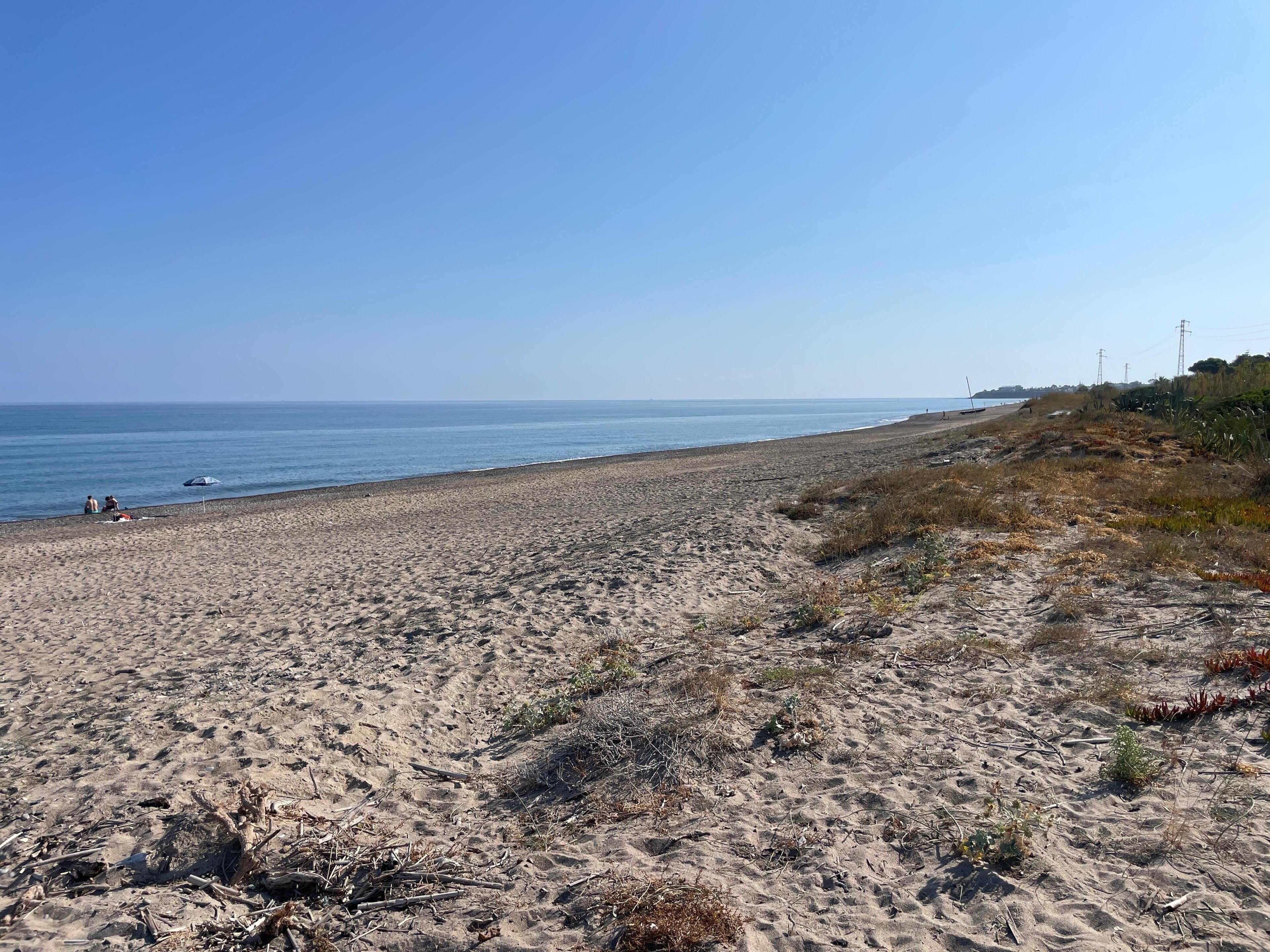 Een zandstrand met een heldere lucht, enkele mensen en in de verte elektriciteitskabels.