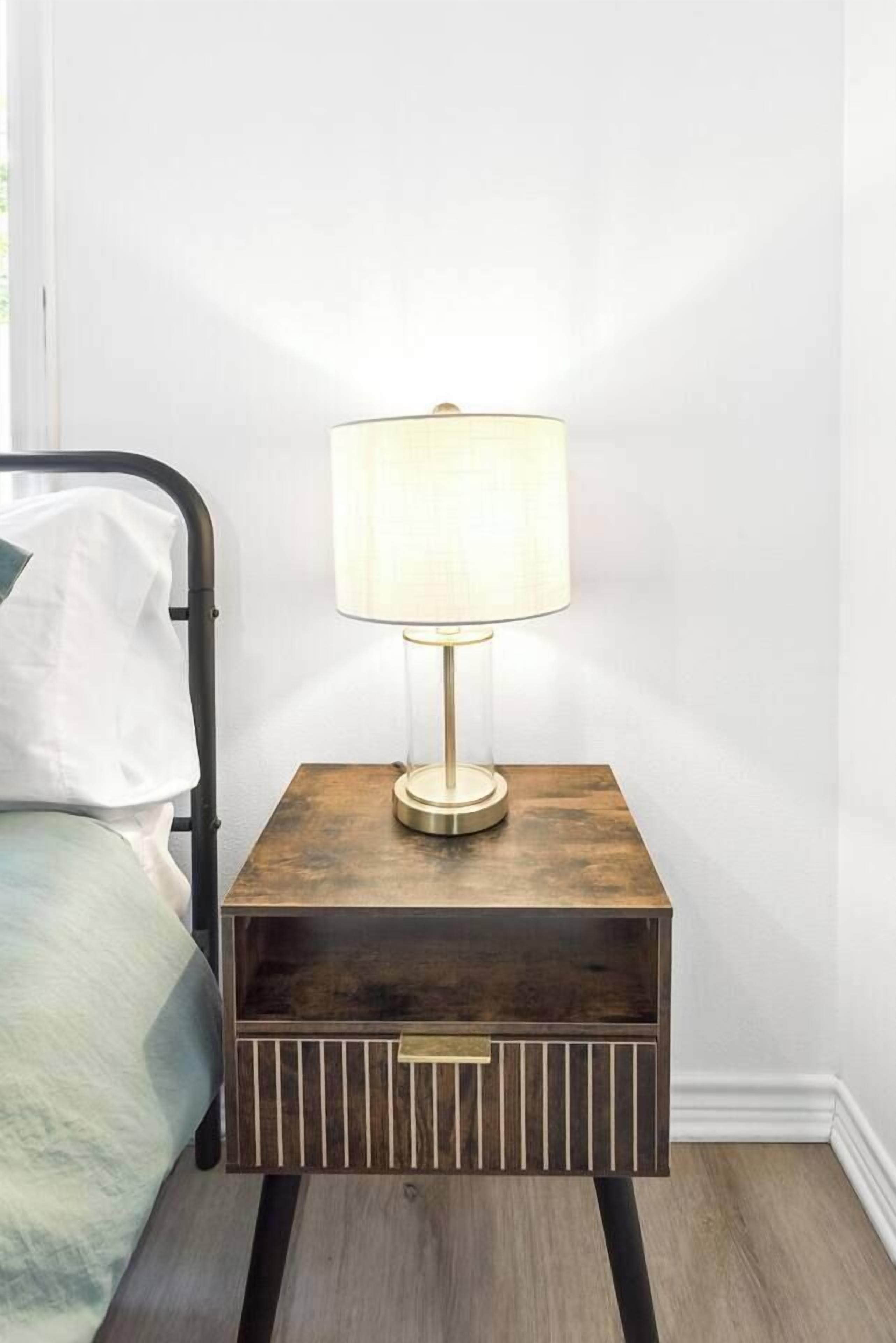 Une table de chevet avec une lampe, un lit avec un oreiller et un plancher en bois.