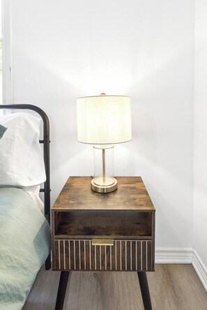 A bedside table with a lamp, a bed with a pillow, and a wooden floor.
