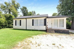 A single-story mobile home with a front porch, a small attached garage, and a well-maintained lawn.