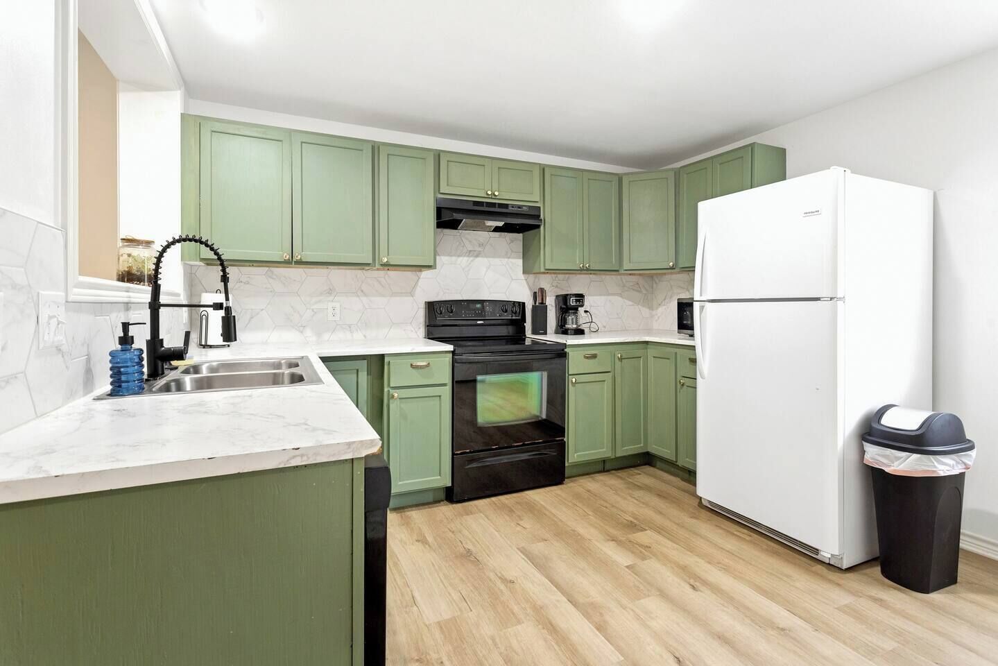 Una cocina compacta con armarios verdes, un refrigerador blanco y una estufa negra.
