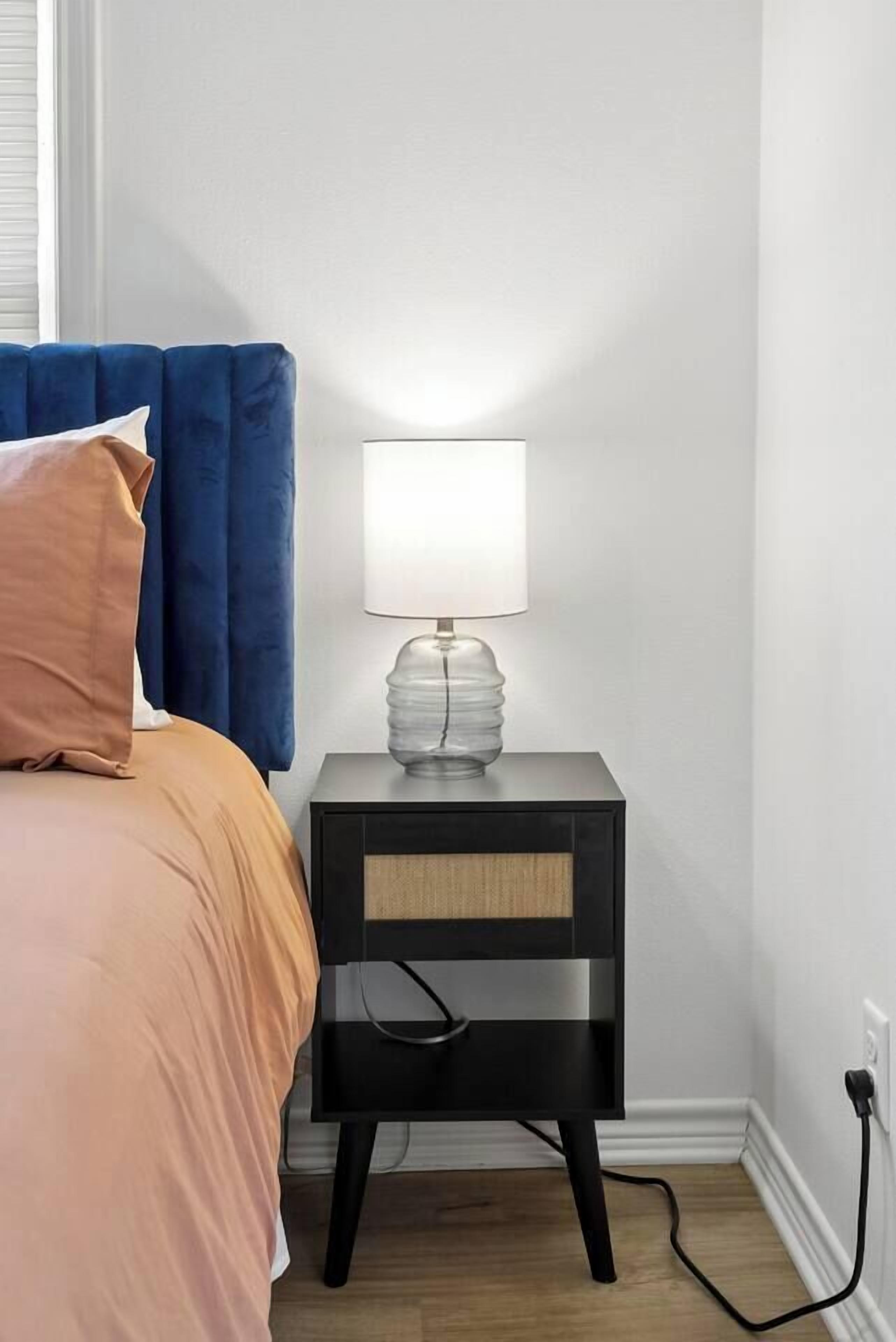 Un lit avec une tête de lit bleue, une lampe de chevet et une table de chevet noire avec un câble.