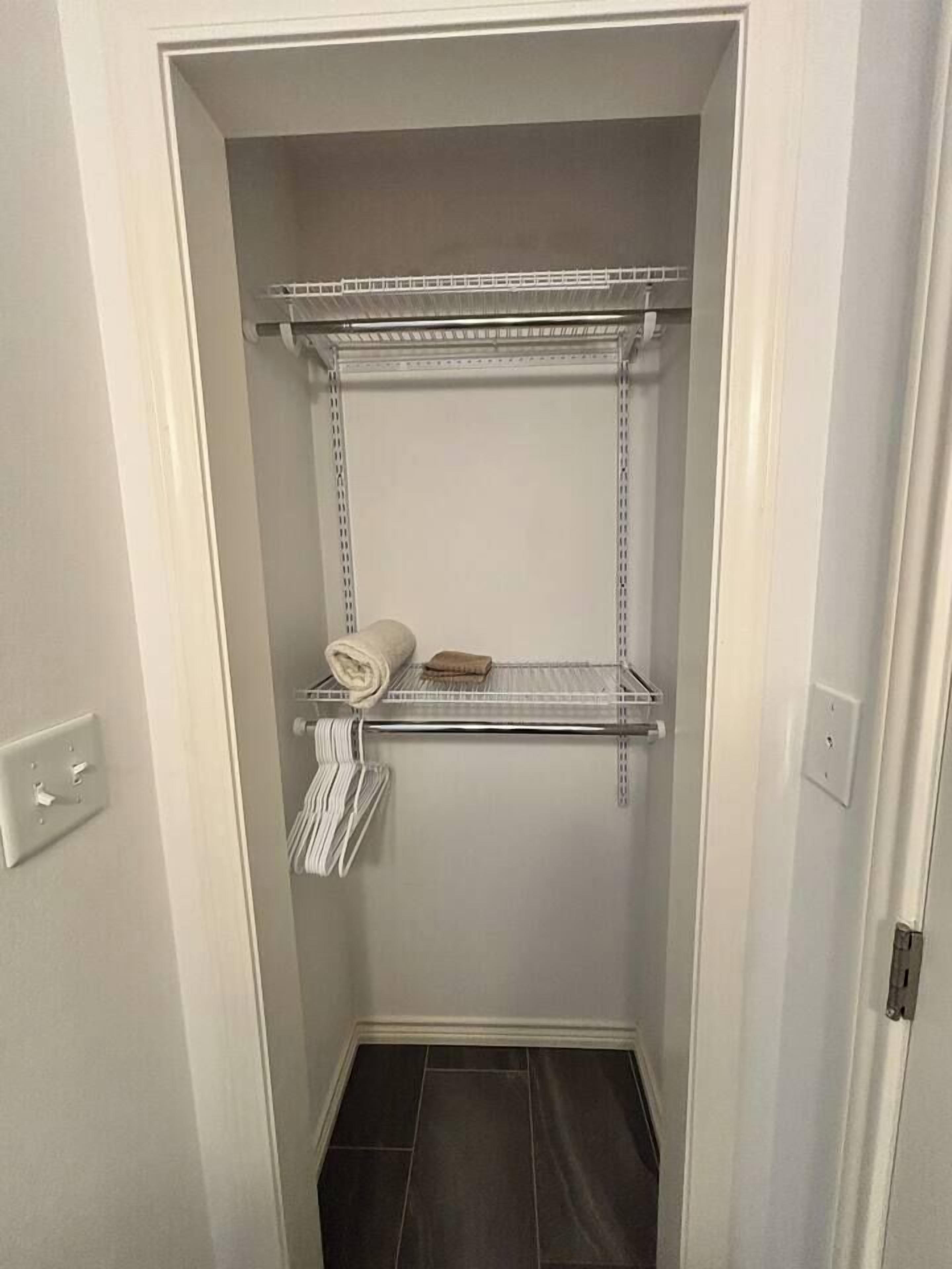 A narrow walk-in closet with metal shelving units, a towel rack, and a small shelf with a folded towel.