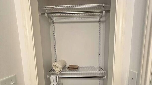 A narrow walk-in closet with metal shelving units, a towel rack, and a small shelf with a folded towel.