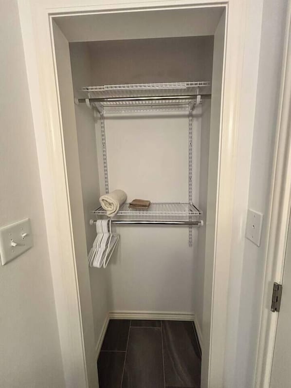 A narrow walk-in closet with metal shelving units, a towel rack, and a small shelf with a folded towel.