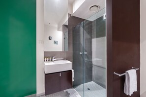 Une salle de bain moderne avec une douche à parois de verre, un lavabo blanc et un meuble-lavabo de couleur foncée.