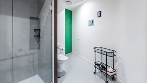 A modern bathroom with a glass shower enclosure, a toilet, and a black metal cart with a white towel. - Skyline Terrace Central CBD Escape with City Views (Melbourne)