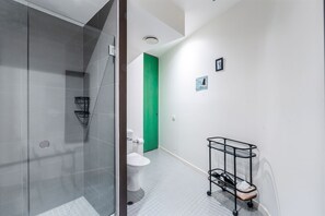 A modern bathroom with a glass shower enclosure, a toilet, and a black metal cart with a white towel. - Skyline Terrace Central CBD Escape with City Views (Melbourne)