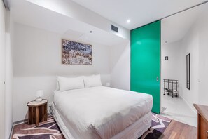 A modern hotel room with a bed, a bedside table, a lamp, a green door, and a painting on the wall. - Skyline Terrace Central CBD Escape with City Views (Melbourne)