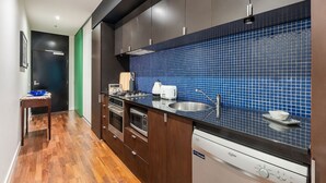 A modern kitchen with dark cabinetry, a blue tiled backsplash, stainless steel appliances, and a wooden floor. - Skyline Terrace Central CBD Escape with City Views (Melbourne)