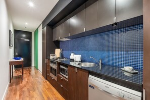 A modern kitchen with dark cabinetry, a blue tiled backsplash, stainless steel appliances, and a wooden floor. - Skyline Terrace Central CBD Escape with City Views (Melbourne)