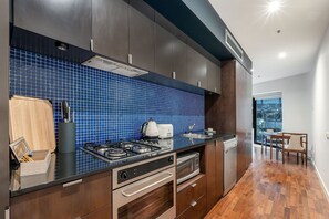 A modern kitchen with a blue tiled backsplash, stainless steel appliances, and wooden cabinetry. - Skyline Terrace Central CBD Escape with City Views (Melbourne)