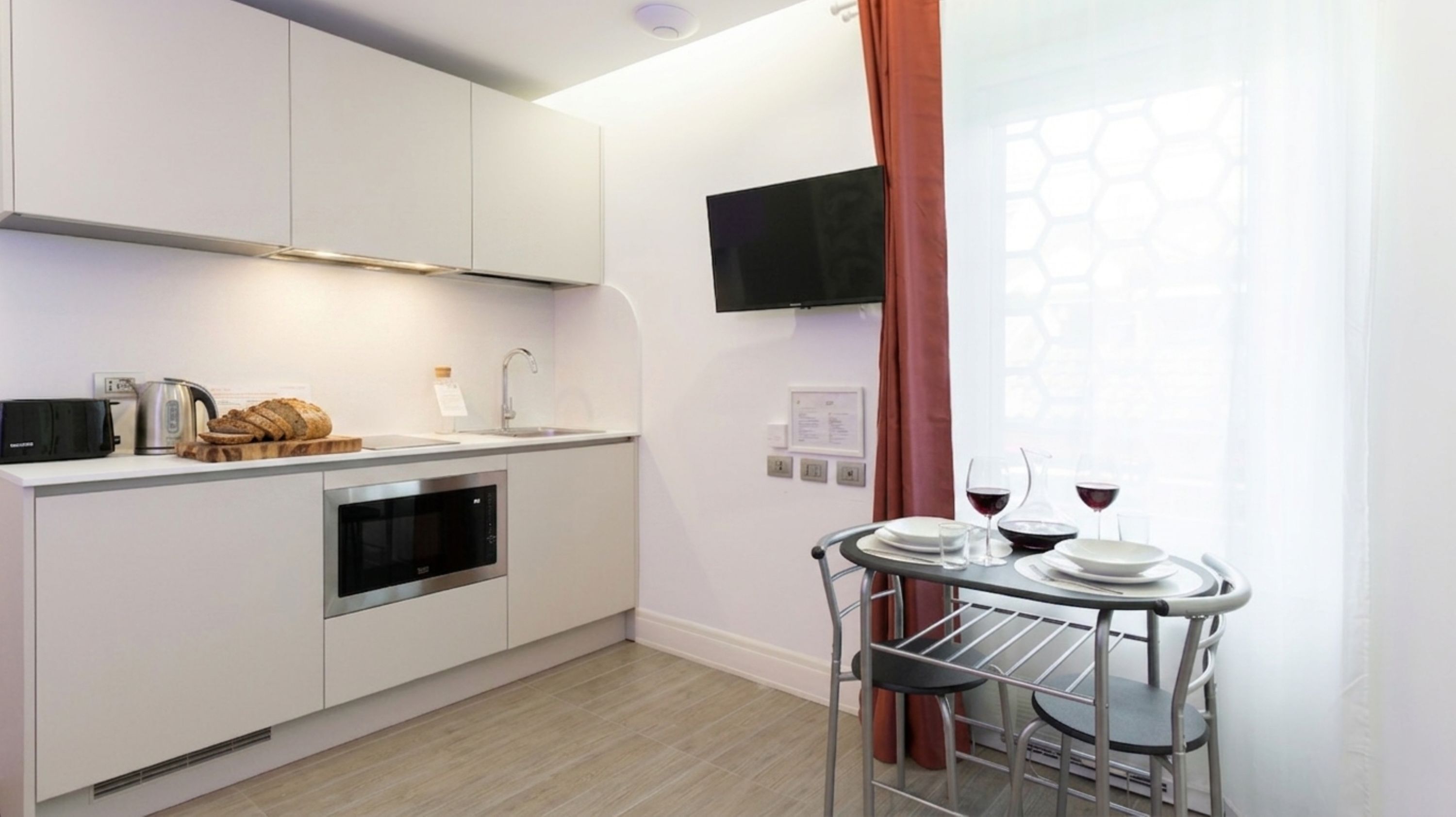 Cocina moderna con armarios blancos, horno integrado, microondas y una pequeña zona de comedor con mesa y sillas.