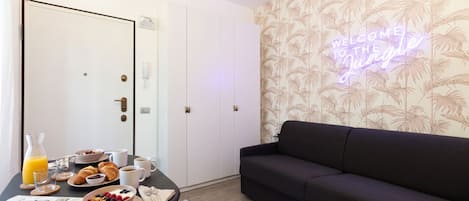A room with a dining table set for breakfast, a sofa, and a neon sign on the wall.