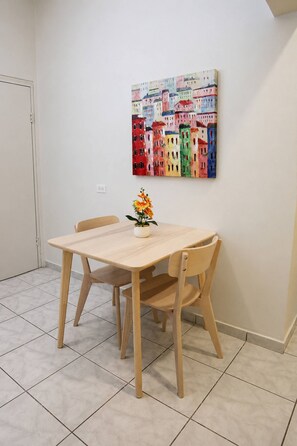 A dining area with a wooden table and chairs, a vase with flowers, and a colorful cityscape painting on the wall. - Cozy 1br Minutes Walking from Escambron Beach (San Juan)
