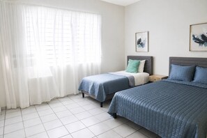 Ein Hotelzimmer mit zwei Betten, einem großen Fenster mit transparenten Vorhängen und einem Fliesenboden.