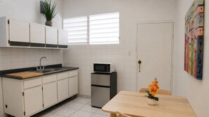 Una cucina compatta con lavello, forno a microonde e frigorifero. C'è un tavolo da pranzo con sedie e un vaso con fiori.