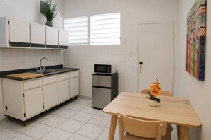 Eine kompakte Küche mit Spüle, Mikrowelle und Kühlschrank. Ein Esstisch mit Stühlen und eine Vase mit Blumen sind ebenfalls vorhanden.
