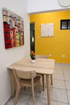 A dining area with a wooden table and chairs, a vase with flowers, and two artworks on the wall. - Cozy 1br Minutes Walking from Escambron Beach (San Juan)