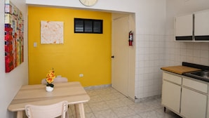 Una cucina con una parete gialla, un orologio, un estintore e una zona pranzo con tavolo e sedie.