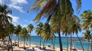 A beach with palm trees, a lifeguard tower, and people relaxing. - Cozy 1br Minutes Walking from Escambron Beach (San Juan)