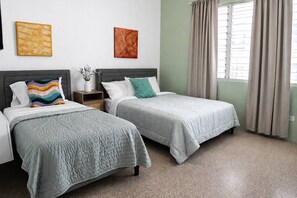 Quarto de hotel com duas camas, uma mesa de cabeceira, um vaso com flores e obras de arte nas paredes.