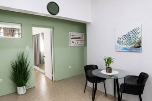 A room with a green wall, a clock, a painting, a potted plant, and a table with chairs. - 1BR Near Escambrón Beach & Old San Juan (San Juan)