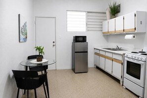 A compact kitchen with a refrigerator, microwave, stove, and sink. There is a dining table with chairs and a small potted plant. - 1BR Near Escambrón Beach & Old San Juan (San Juan)