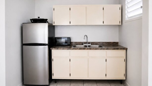 Cocina compacta con refrigerador de acero inoxidable, microondas, pileta y alacenas de tonos claros.
