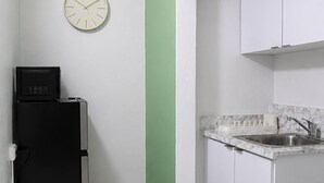 Eine Küche mit weißen Schränken, einem schwarzen Kühlschrank, einer Uhr an der Wand und einer Wand in Grünton.