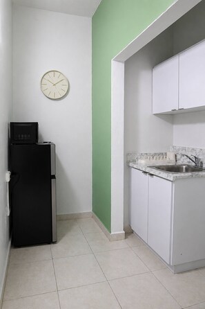 Eine Küche mit weißen Schränken, einem schwarzen Kühlschrank, einer Uhr an der Wand und einer Wand in Grünton.