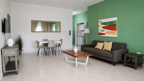 Ein modernes Wohnzimmer mit Essbereich, einer Couch, einem Couchtisch und einem Fernseher.