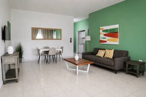 Ein modernes Wohnzimmer mit Essbereich, einer Couch, einem Couchtisch und einem Fernseher.