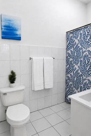 Ein Badezimmer mit Toilette, Waschbecken, einer Dusche mit blau gemustertem Vorhang und einem kleinen Blumentopf.