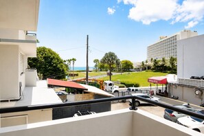 A view from a balcony overlooking a parking area with a Tropical Coffee sign, a grassy area, and a building with a grid-like facade. - Spacious Budget-Friendly 1BR by Escambron Beach (San Juan)