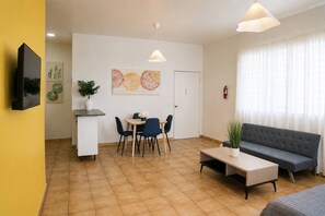 A modern living room with a sofa, coffee table, and dining area with chairs. There is a fire extinguisher on the wall and a plant on the coffee table. - Spacious Budget-Friendly 1BR by Escambron Beach (San Juan)