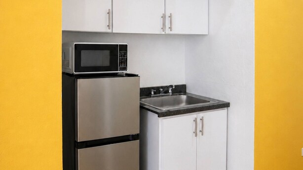 Ett kompakt kök med mikrovågsugn, spis och skåp mot en gul vägg.