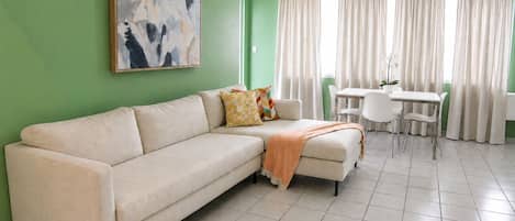 A living room with a sofa, a coffee table, and a dining area with chairs and curtains.