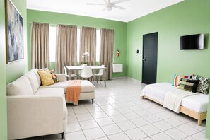 A modern living room with a sofa, a bed, a dining area with chairs, and a TV mounted on the wall. - Vibrant 1BR w Balcony, Steps to Escambron Beach (San Juan)