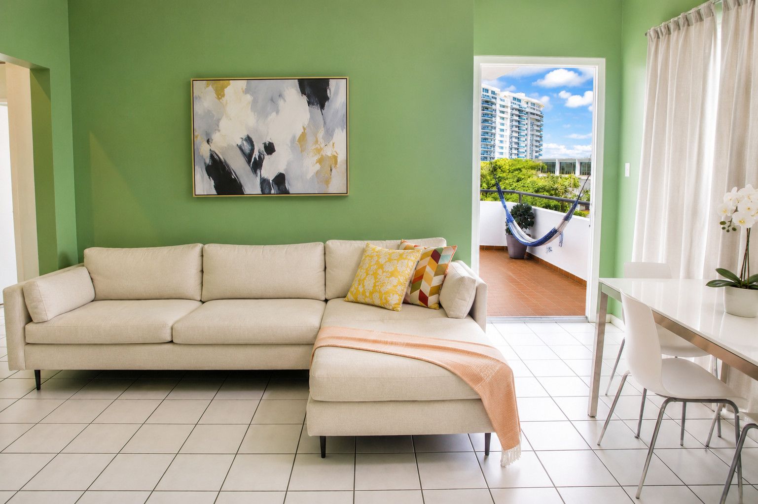 Una sala de estar con un sofá color beige, un cuadro en la pared y vistas a un balcón con una hamaca.