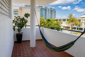 A balcony with a hammock, potted plant, and a view of a modern building. - Vibrant 1BR w Balcony, Steps to Escambron Beach (San Juan)