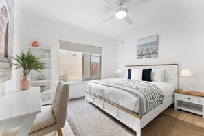 Une chambre à coucher moderne avec un lit, des tables de chevet, un bureau, une chaise, une plante en pot et une fenêtre.