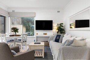Un salon moderne comprenant un canapé, des fauteuils, une table basse, un téléviseur et une fenêtre donnant sur un paysage verdoyant.