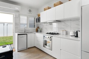 Ett modernt kök med vita köksskåp, en inbyggd diskmaskin, en spis och en kaffebryggare.