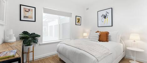 Um quarto moderno com uma cama grande, um ventilador de teto, uma janela e obras de arte nas paredes.