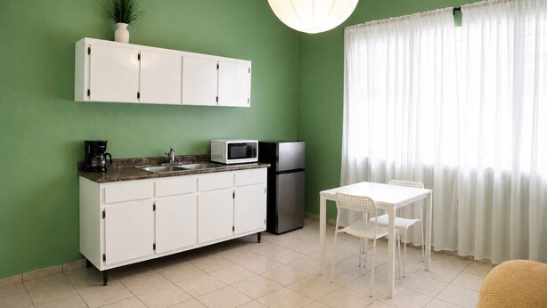 A kitchen with white cabinets, a microwave, a refrigerator, a coffee maker, and a dining table with chairs. - Charming 1 BR Walking Distance to Escambron Beach (San Juan)