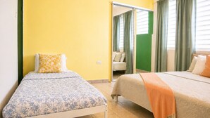 A room with two beds, one with a floral bedspread and the other with a solid color bedspread. There is a green curtain and a mirror on the wall. - Charming 1 BR Walking Distance to Escambron Beach (San Juan)