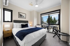 A hotel room with a bed, bedside table, lamp, and a large window with a view of trees and buildings. - Colley Escape Vibrant Life on Glenelgs Foreshore (Glenelg)